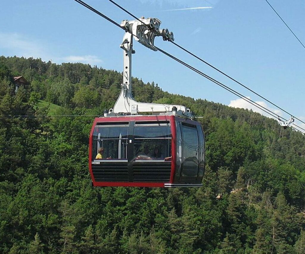 Ovovia panoramica moderna sopra foresta verde, con cielo azzurro e cabina sospesa.