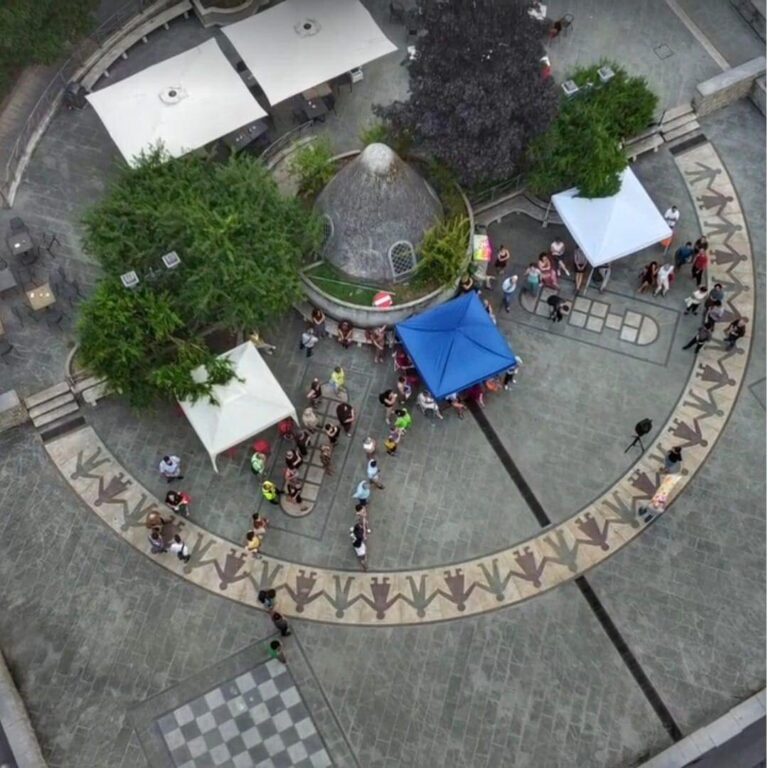 Veduta aerea di piazza circolare con tende, alberi e persone durante un evento allaperto.