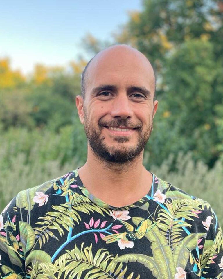 Ritratto outdoor di uomo sorridente con maglietta tropicale e sfondo naturale sfocato.