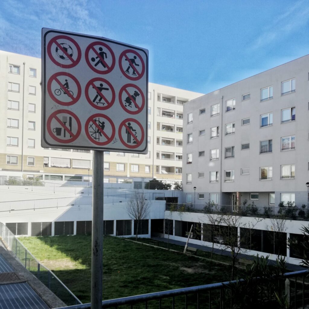 Cartello di divieto con simboli multipli in cortile condominiale moderno con appartamenti e area verde.