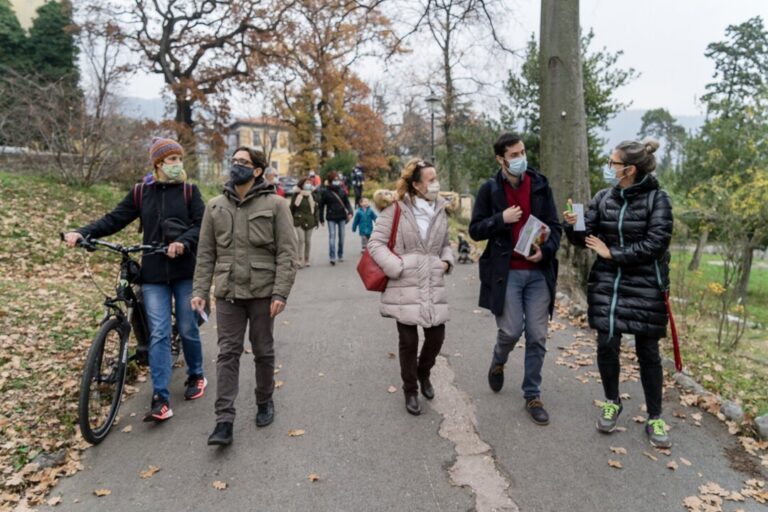 Gruppo in passeggiata autunnale nel parco, con biciclette e bastone da cammino.
