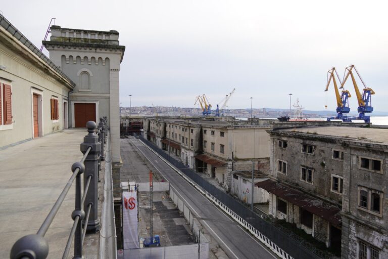 Terrazza panoramica sul quartiere portuale con strada storica e gru industriali sullo sfondo.