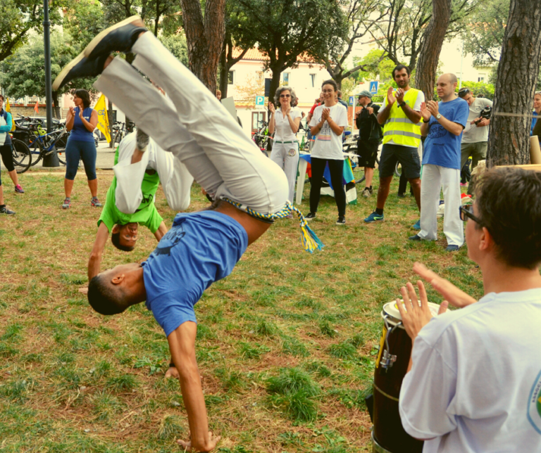 Capoeira nel parco: acrobazia su una mano, pubblico attorno e ritmo di tamburo dal vivo.