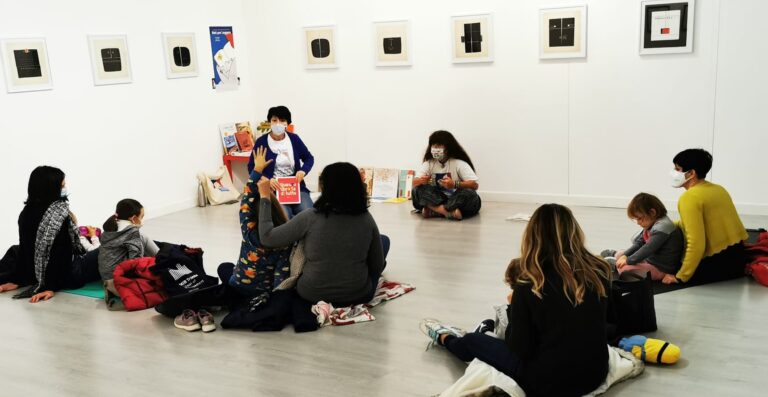 Bambini in laboratorio d’arte al museo, seduti in cerchio tra quadri e materiali didattici.