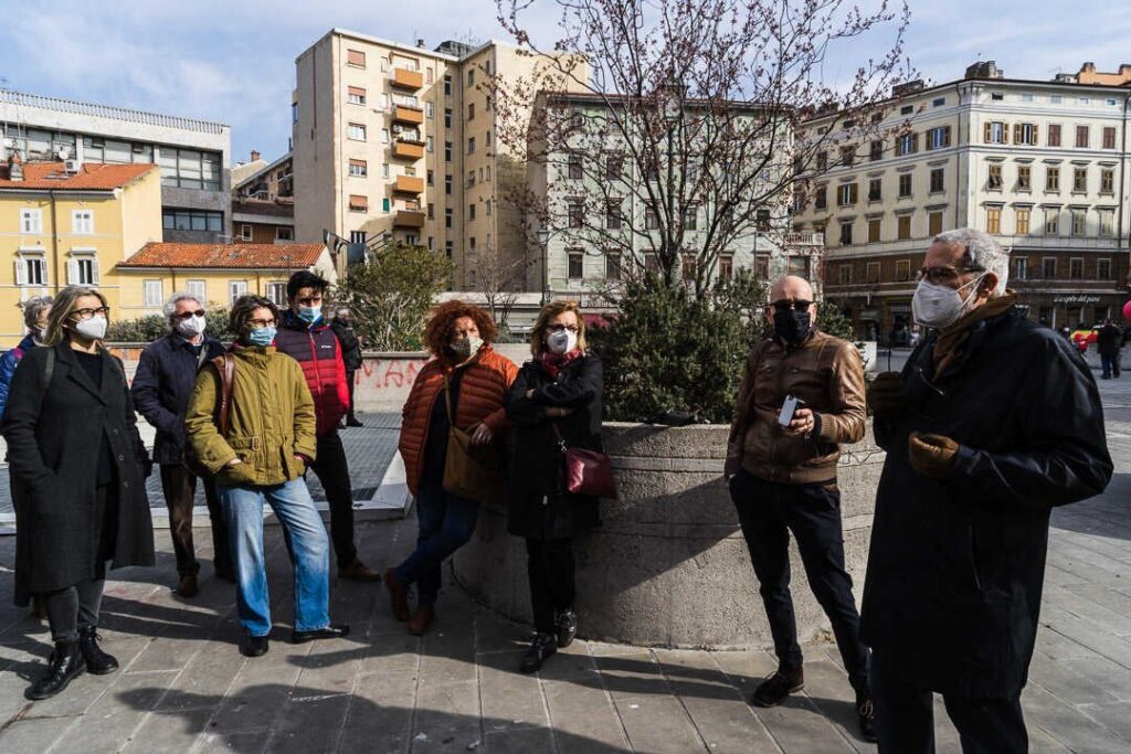 Gruppo in piazza cittadina d’inverno, con mascherine e cappotti, durante un incontro all’aperto.