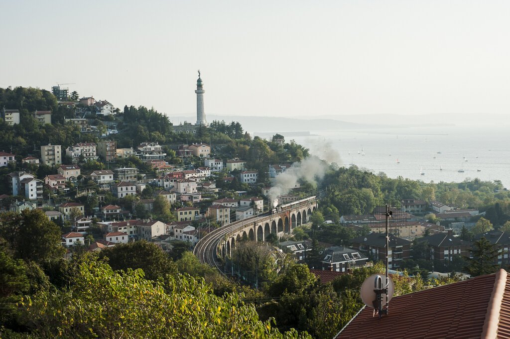 Borgo costiero su collina con viadotto ad archi e mare.