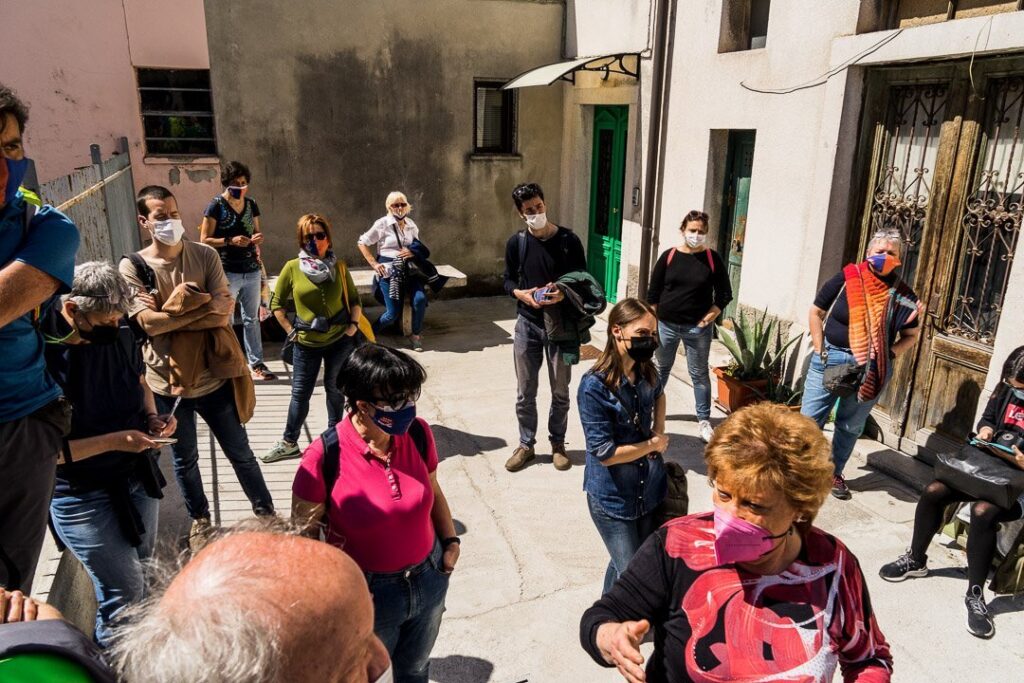 Gruppo con mascherina in cortile urbano soleggiato durante visita guidata.