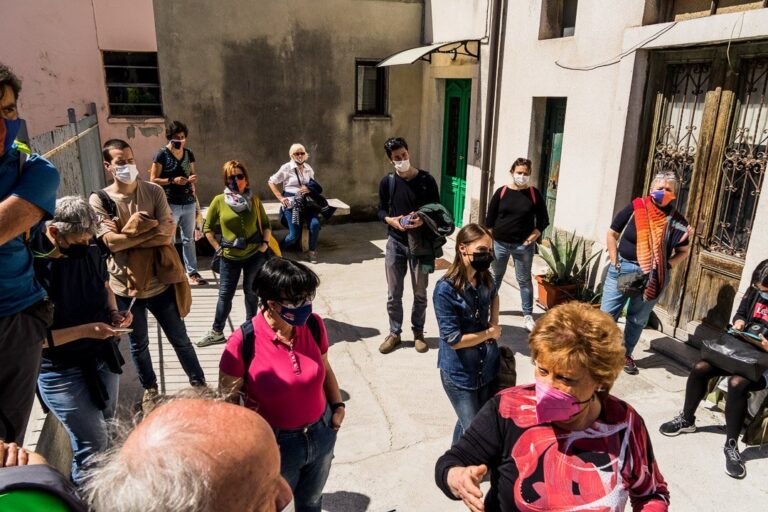 Gruppo con mascherina in cortile urbano soleggiato durante visita guidata.