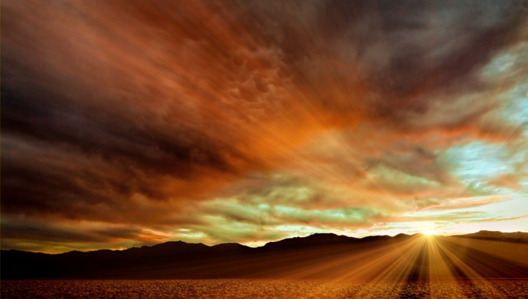 Tramonto epico nel deserto con nuvole tempestose, sole basso e montagne in silhouette.