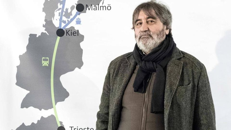 Uomo con barba davanti a mappa ferroviaria europea da Malmö a Trieste.