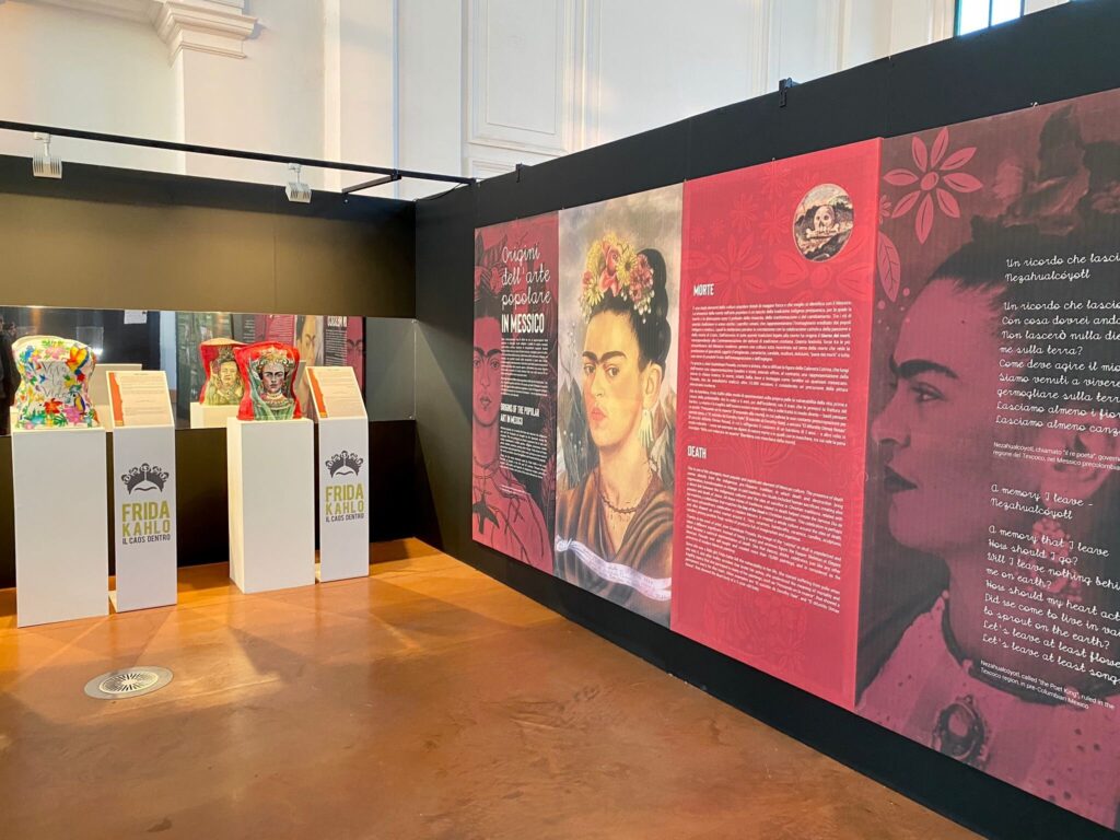 Mostra di Frida Kahlo in galleria moderna con pannelli rossi e teche espositive.