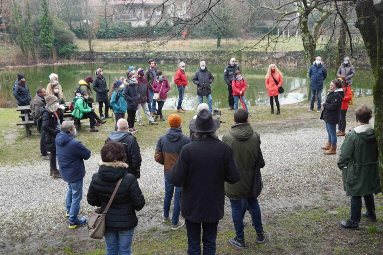 Passeggiata naturalistica sul fiume con guida in giacca arancione e gruppo di adulti.