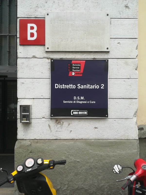 Distretto Sanitario 2 su facciata pubblica con ingresso laterale e scooter parcheggiati.