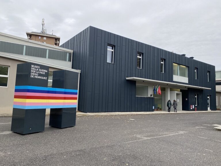 Museo Henriquez: facciata moderna scura, insegna colorata e ingresso sotto cielo nuvoloso.