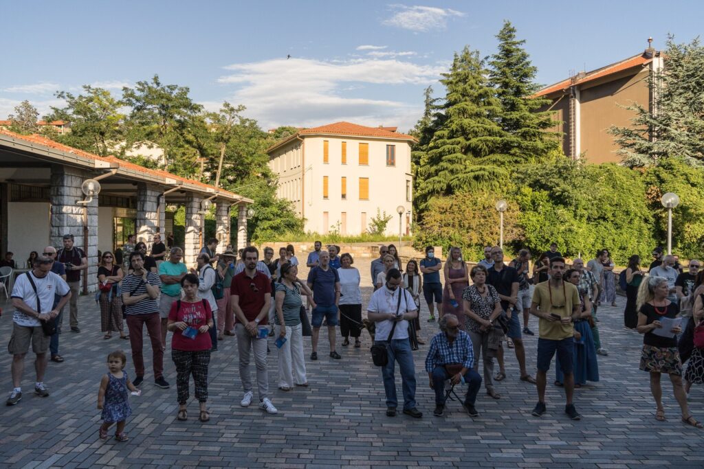 Piazza storica mediterranea con folla di turisti, edifici antichi e luce calda.