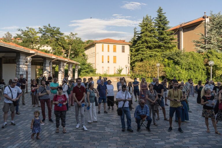 Piazza storica mediterranea con folla di turisti, edifici antichi e luce calda.
