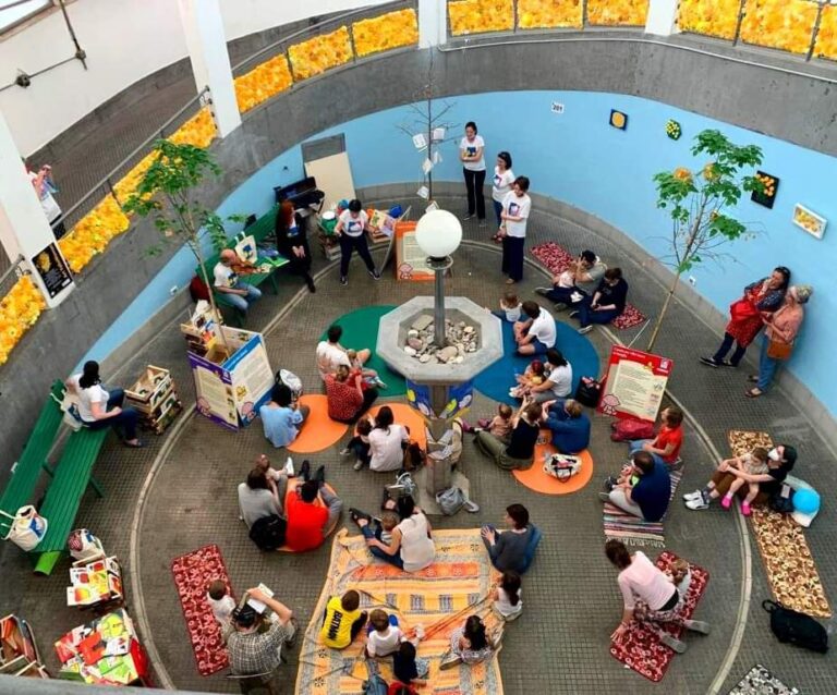 Area giochi indoor per bambini e famiglie con lettura, tappeti e attività condivise.