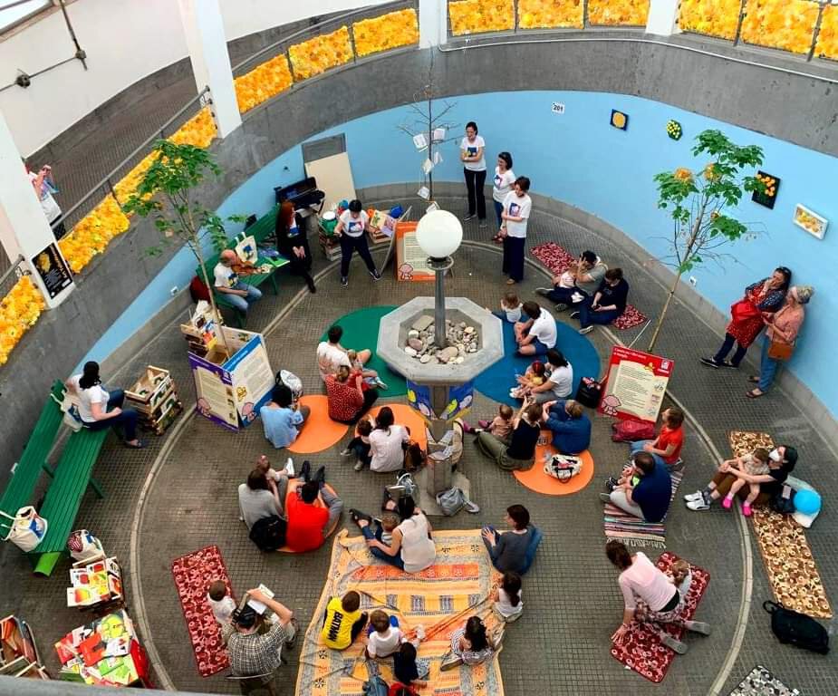 Area giochi indoor per bambini e famiglie con lettura, tappeti e attività condivise.