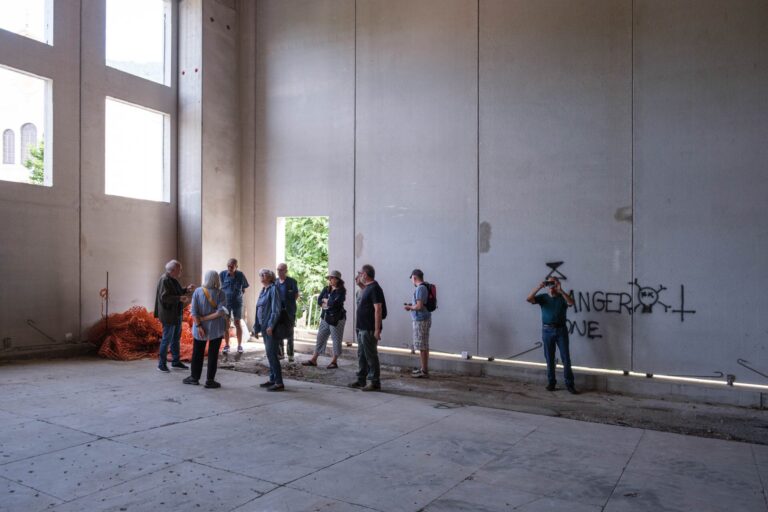 Interno industriale vuoto con gruppo di persone, graffiti e luce naturale.