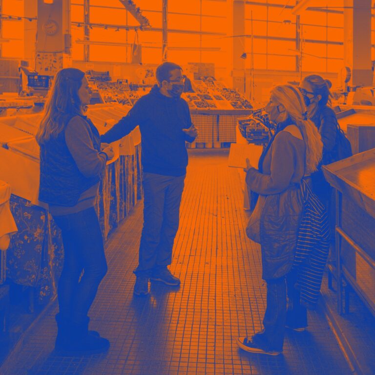 Gruppo in cucina industriale durante visita guidata tra attrezzature e superfici in acciaio.