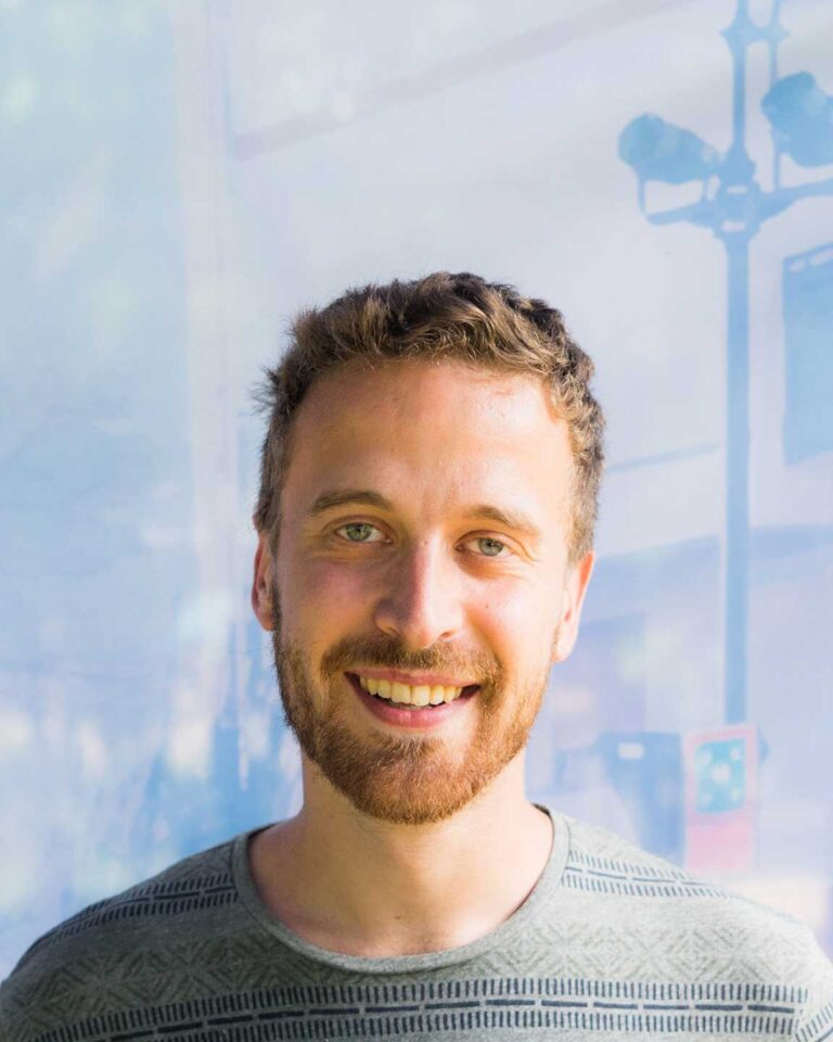 Ritratto ravvicinato di Kevin Nicolini sorridente, con barba curata e maglione verde grigio.