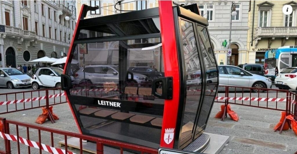 Cabina funivia LEITNER esposta in città, con vetri scuri e dettagli rossi.