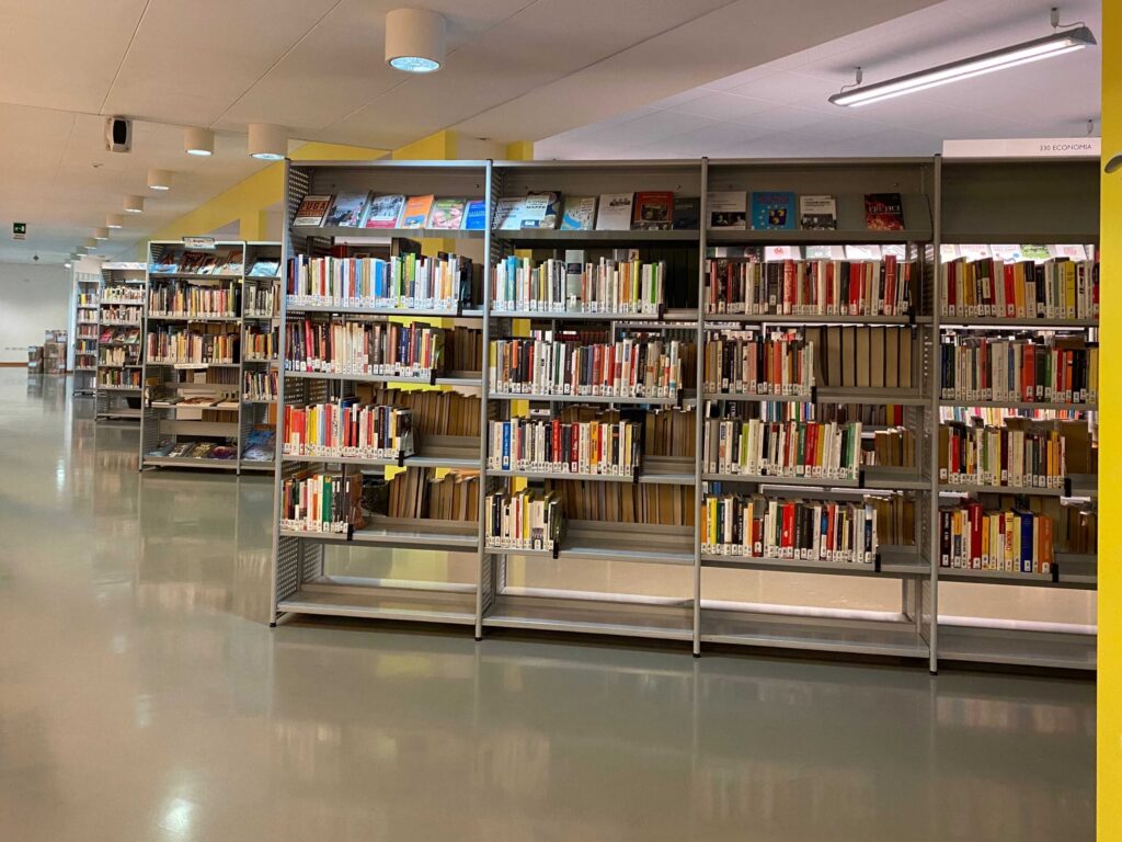 Interno di biblioteca moderna con scaffali metallici pieni di libri e corridoio spazioso.