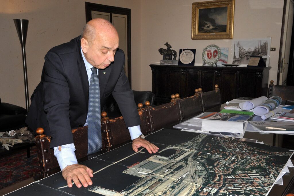 Uomo in ufficio esamina mappe e planimetrie su un grande tavolo.