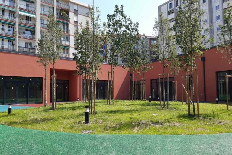 Cortile condominiale moderno con prato, giovani alberi e palazzi residenziali soleggiati.