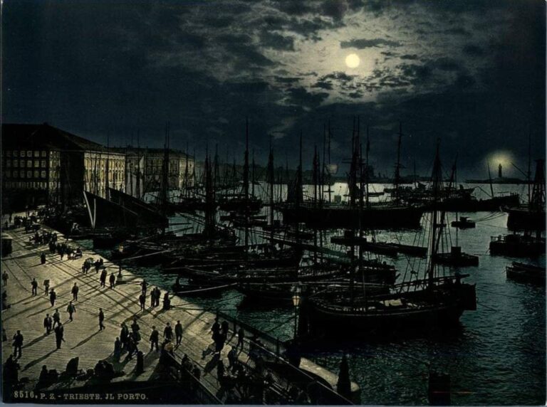 Porto notturno al chiaro di luna con velieri, passeggiata animata e riflessi sull’acqua.