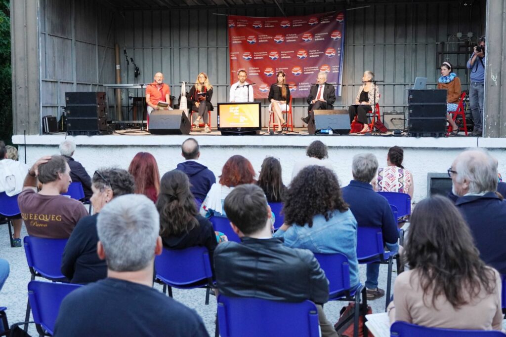 Concerto dal vivo all’aperto con band su palco coperto e pubblico seduto.