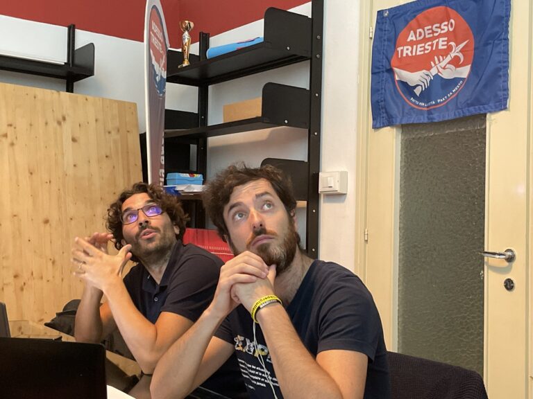 Due amici scherzano in ufficio creativo, seduti vicino alla scrivania con mani giunte.