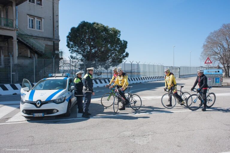 Controllo stradale: polizia e ciclisti in giallo su strada urbana soleggiata.