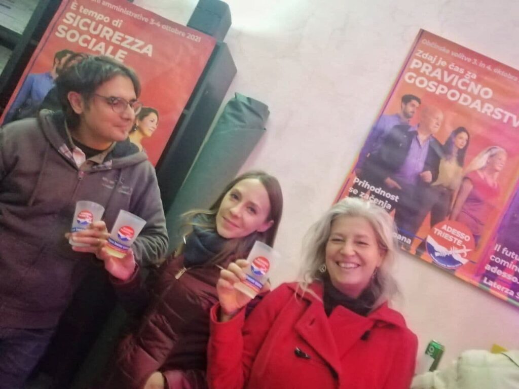 Tre persone con volantini davanti a manifesti politici italiani in una sede interna.