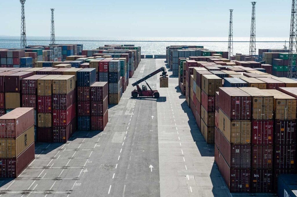 Cantiere container del porto di Trieste con gru, mezzi logistici e mare sullo sfondo.