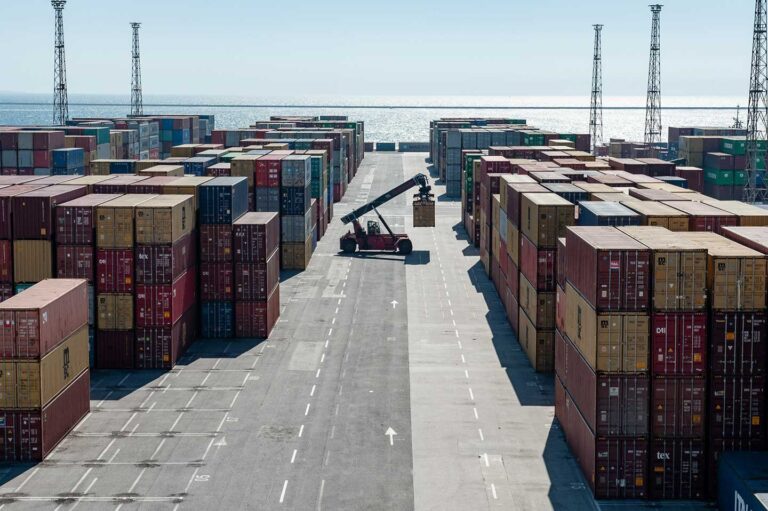 Cantiere container del porto di Trieste con gru, mezzi logistici e mare sullo sfondo.