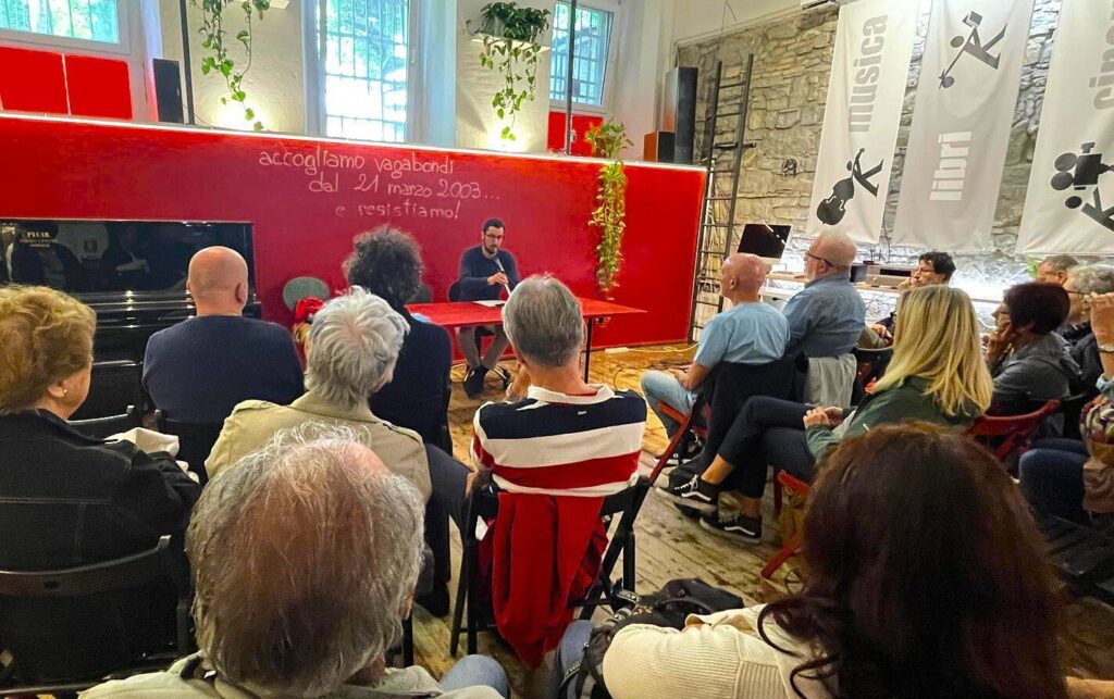 Incontro culturale con pubblico in sala rossa e luminosa