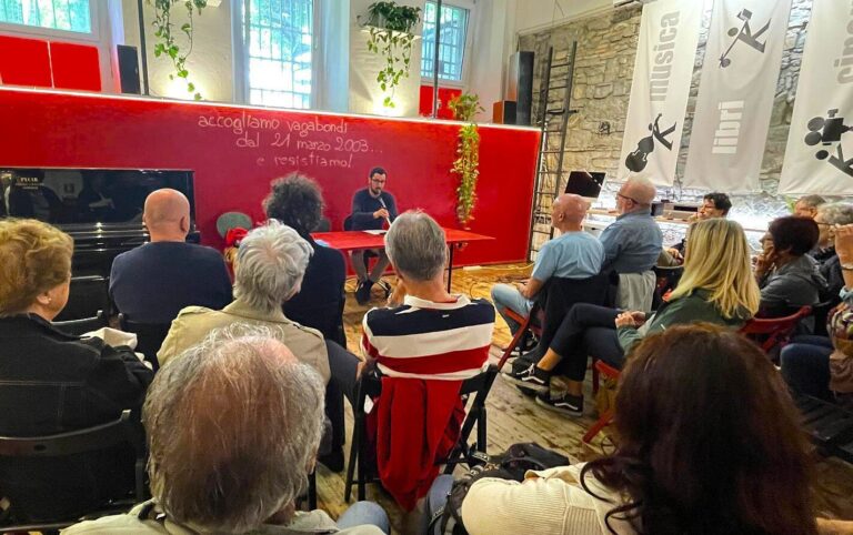 Incontro culturale con pubblico in sala rossa e luminosa