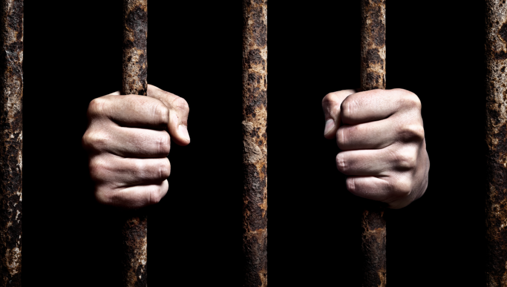 Mani strette su sbarre arrugginite nel buio, simbolo di prigionia e libertà.