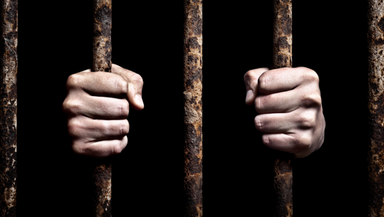 Mani strette su sbarre arrugginite nel buio, simbolo di prigionia e libertà.