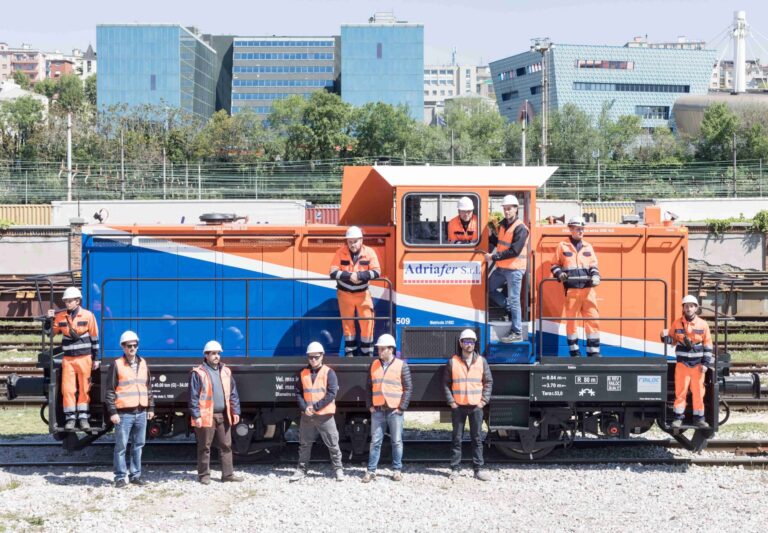 Operai ferroviari in posa su veicolo di manutenzione arancione in deposito industriale.