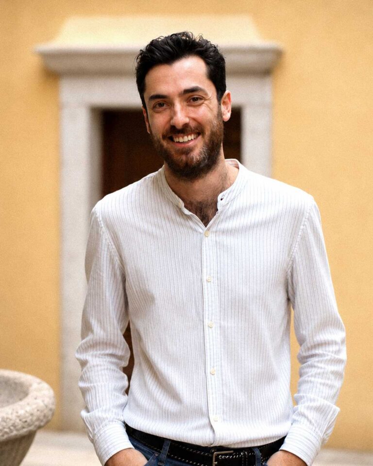 Ritratto outdoor di Riccardo Laterza, sorridente in camicia bianca davanti a parete gialla.