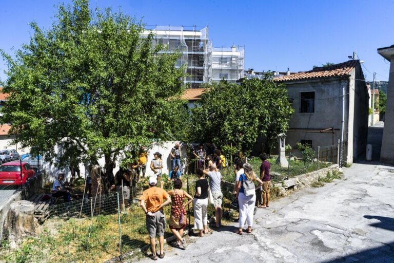 Scena di strada a San Luigi con persone, albero ombreggiante e edifici misti.
