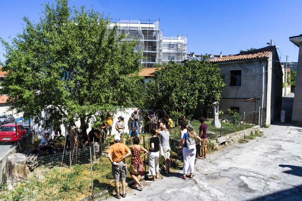 Scena di strada a San Luigi con persone, albero ombreggiante e edifici misti.