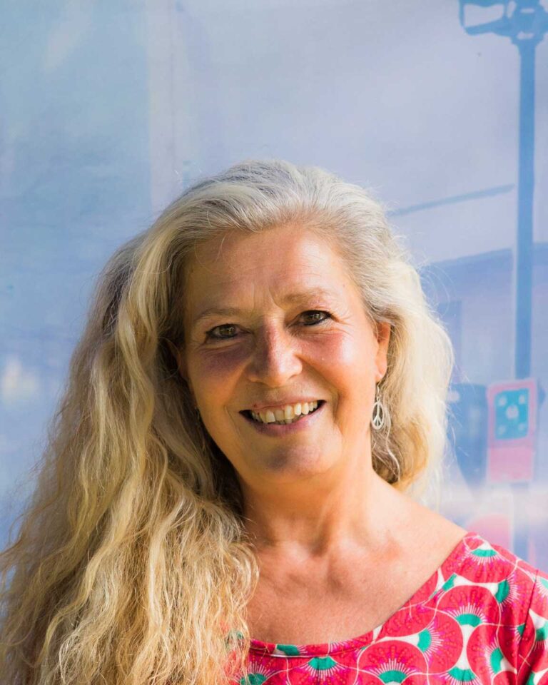 Ritratto di donna sorridente con capelli grigio-blondi e top colorato vivace.