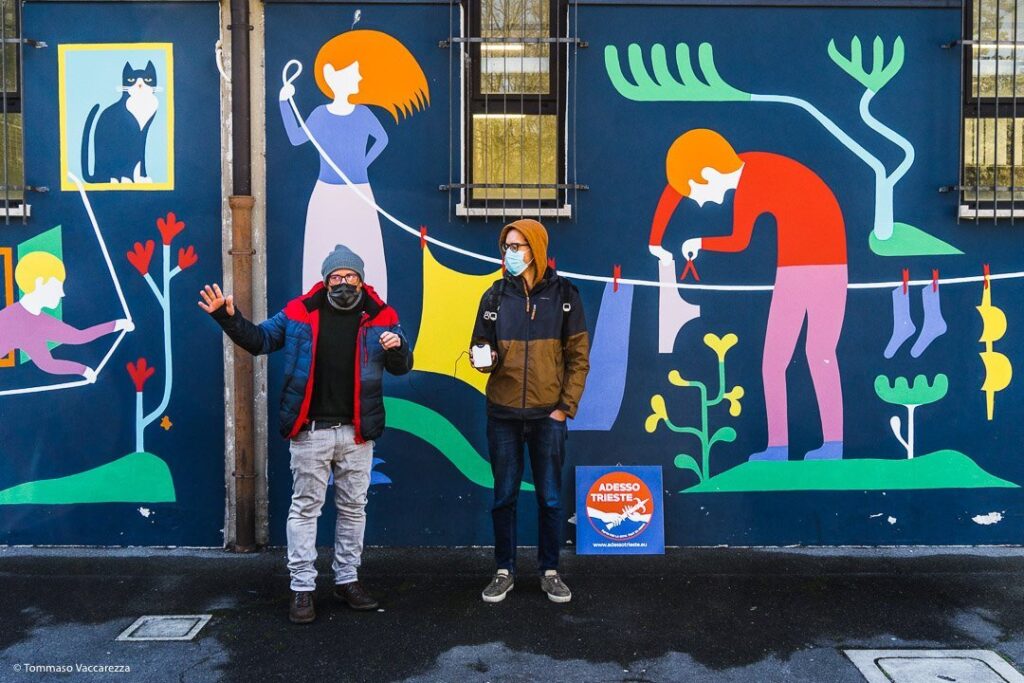 Murale street art colorato con due persone che posano davanti a una parete urbana.