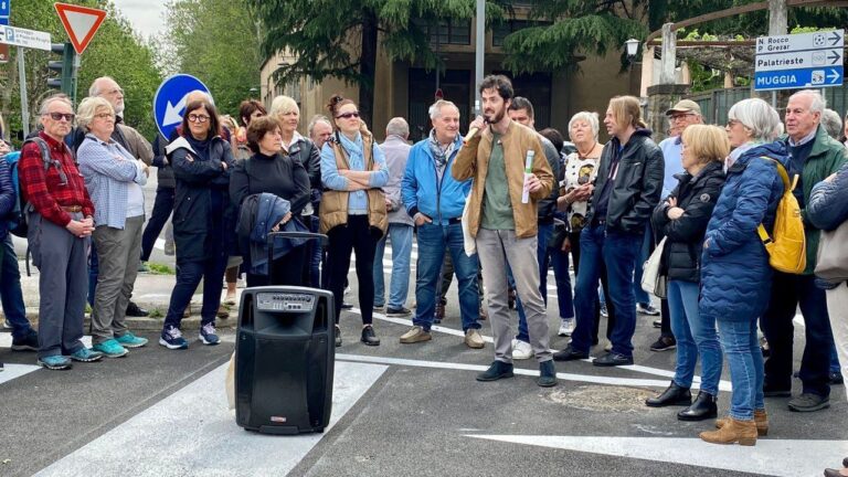 Gruppo ascolta una guida urbana con microfono su un attraversamento pedonale alberato.