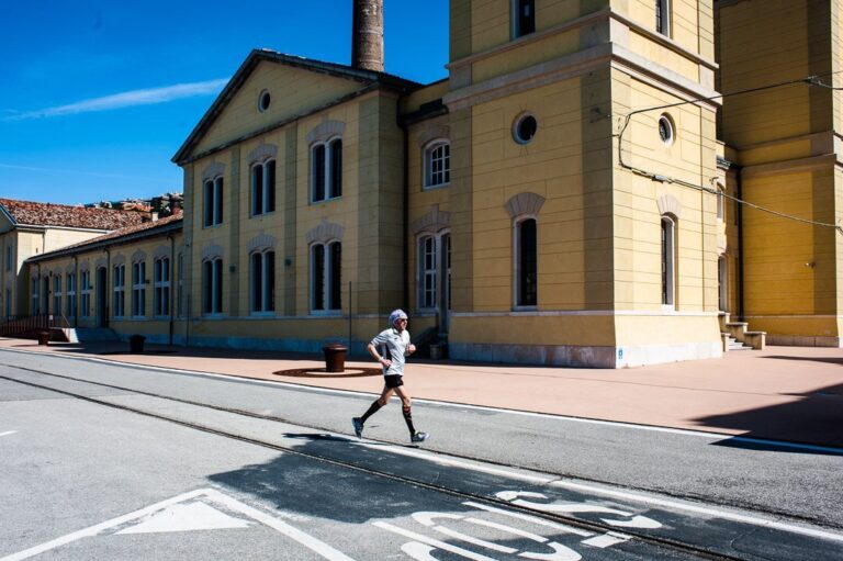 Runner attraversa strada storica assolata accanto a edificio classico giallo e beige.