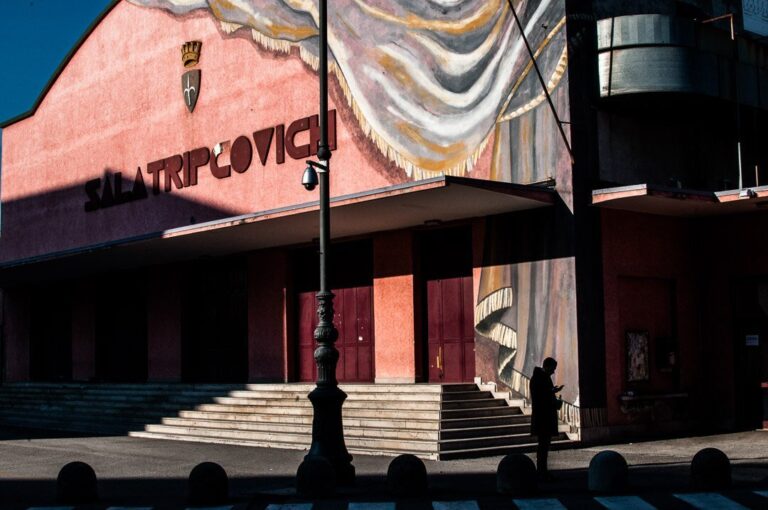 Teatro rosato con sipario decorativo, lampione in primo piano e passante in controluce.