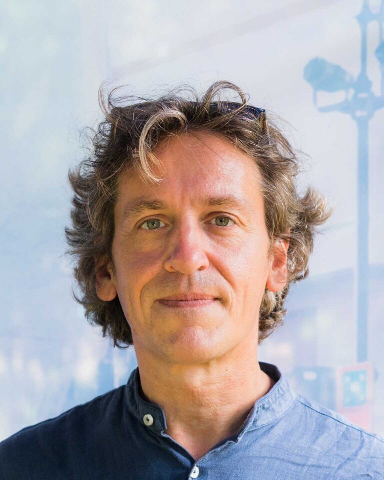 Ritratto naturale di uomo con capelli castani e camicia blu scura, sfondo chiaro.
